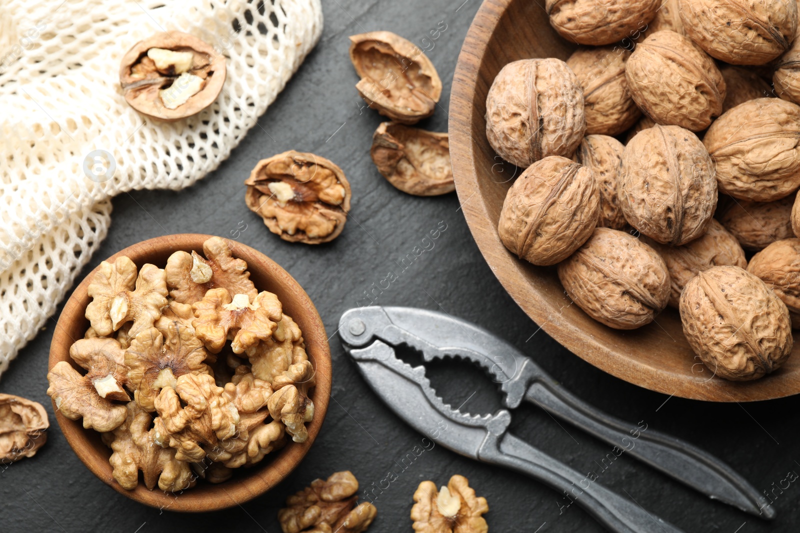 Photo of Fresh ripe walnuts, nutcracker and shells on black table, flat lay