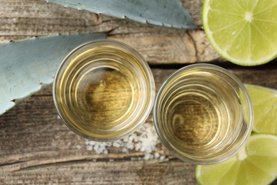 Photo of Mexican tequila shots, slices of lime, salt and agave leaves on wooden table, flat lay