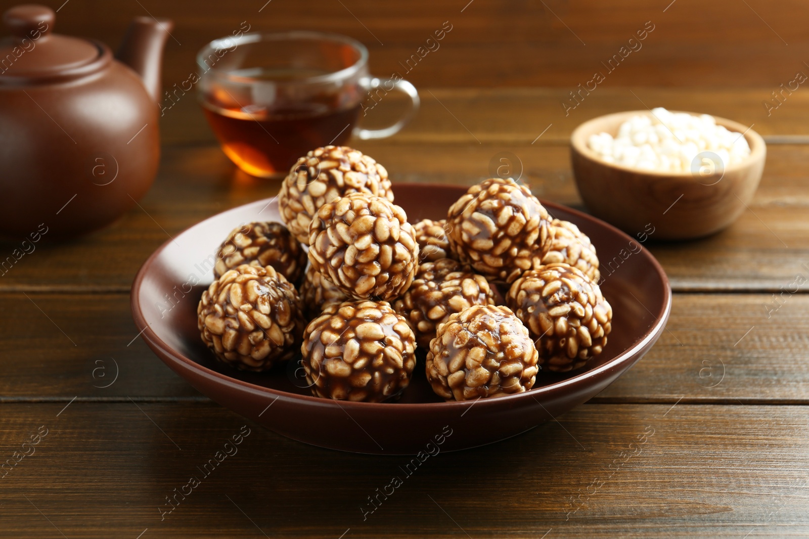 Photo of Delicious chocolate puffed rice balls in bowl and tea on wooden table