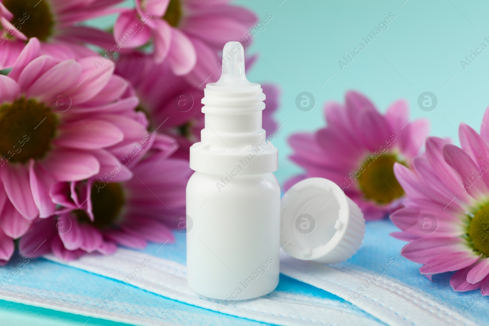 Photo of Allergy treatment. Nasal drops, protective masks and flowers on light blue background, closeup