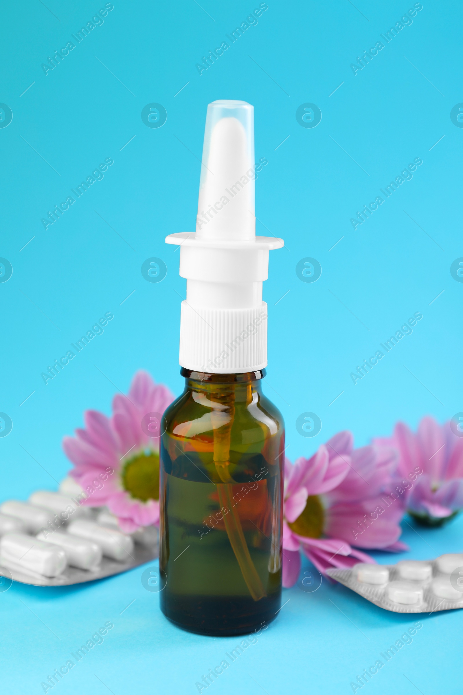 Photo of Allergy treatment. Nasal spray, pills and flowers on light blue background