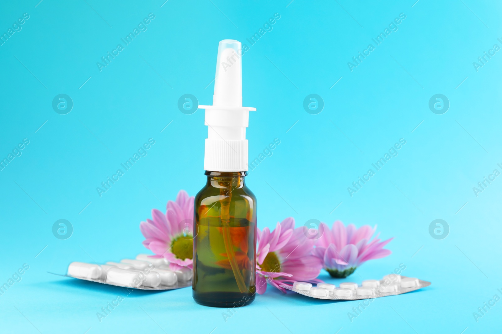 Photo of Allergy treatment. Nasal spray, pills and flowers on light blue background