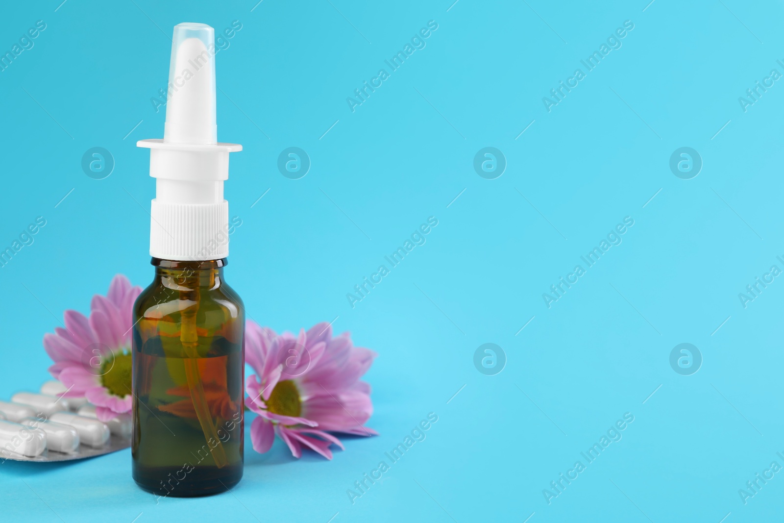 Photo of Allergy treatment. Nasal spray, pills and flowers on light blue background. Space for text