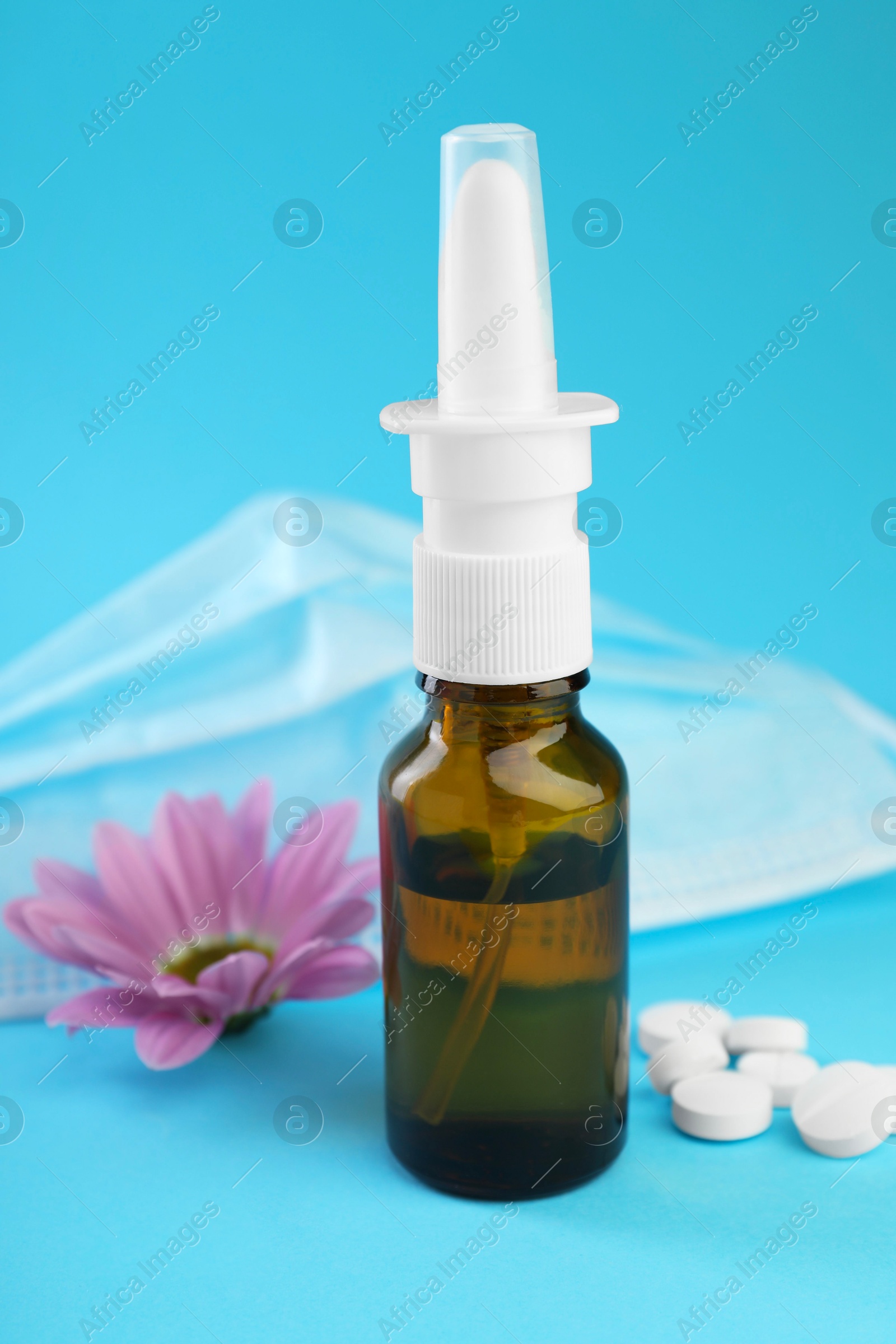 Photo of Allergy treatment. Nasal spray, pills, protective mask and flower on light blue background