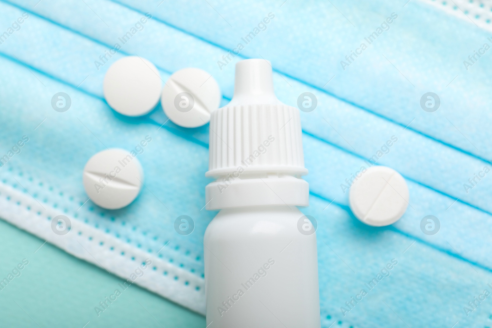 Photo of Allergy treatment. Nasal drops, pills and protective mask on light blue background, closeup