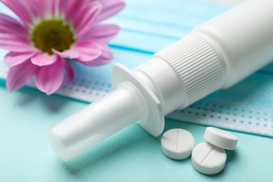 Photo of Allergy treatment. Nasal spray, pills and flower on light blue background, closeup