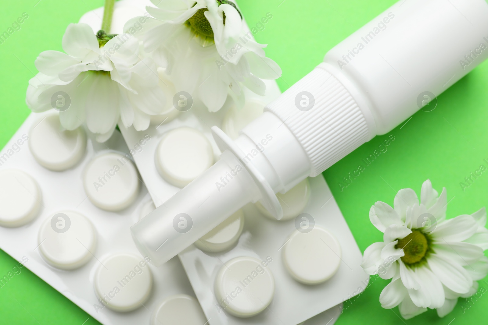 Photo of Allergy treatment. Nasal spray, pills and flowers on green background, closeup