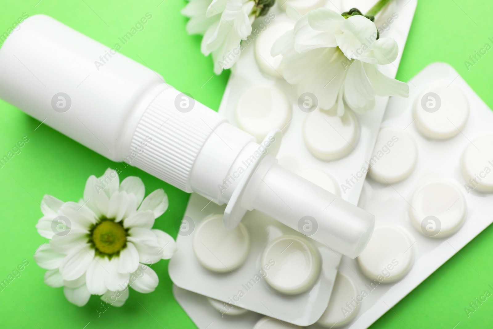 Photo of Allergy treatment. Nasal spray, pills and flowers on green background, closeup