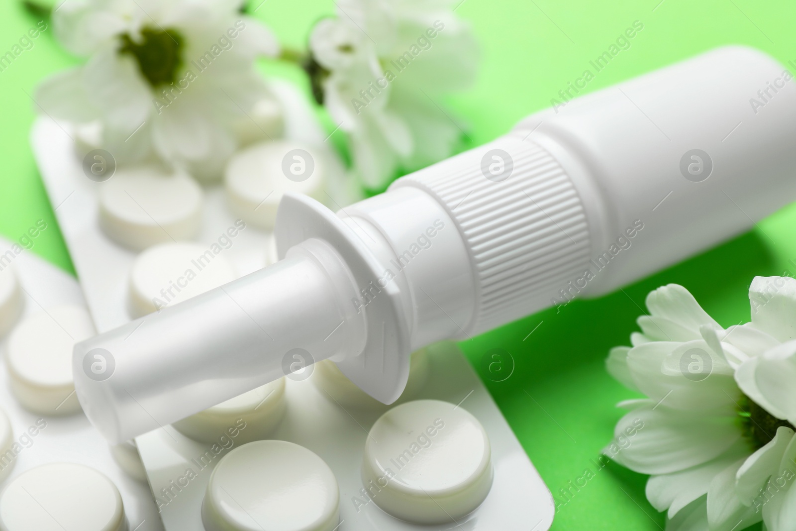 Photo of Allergy treatment. Nasal spray, pills and flowers on green background, closeup