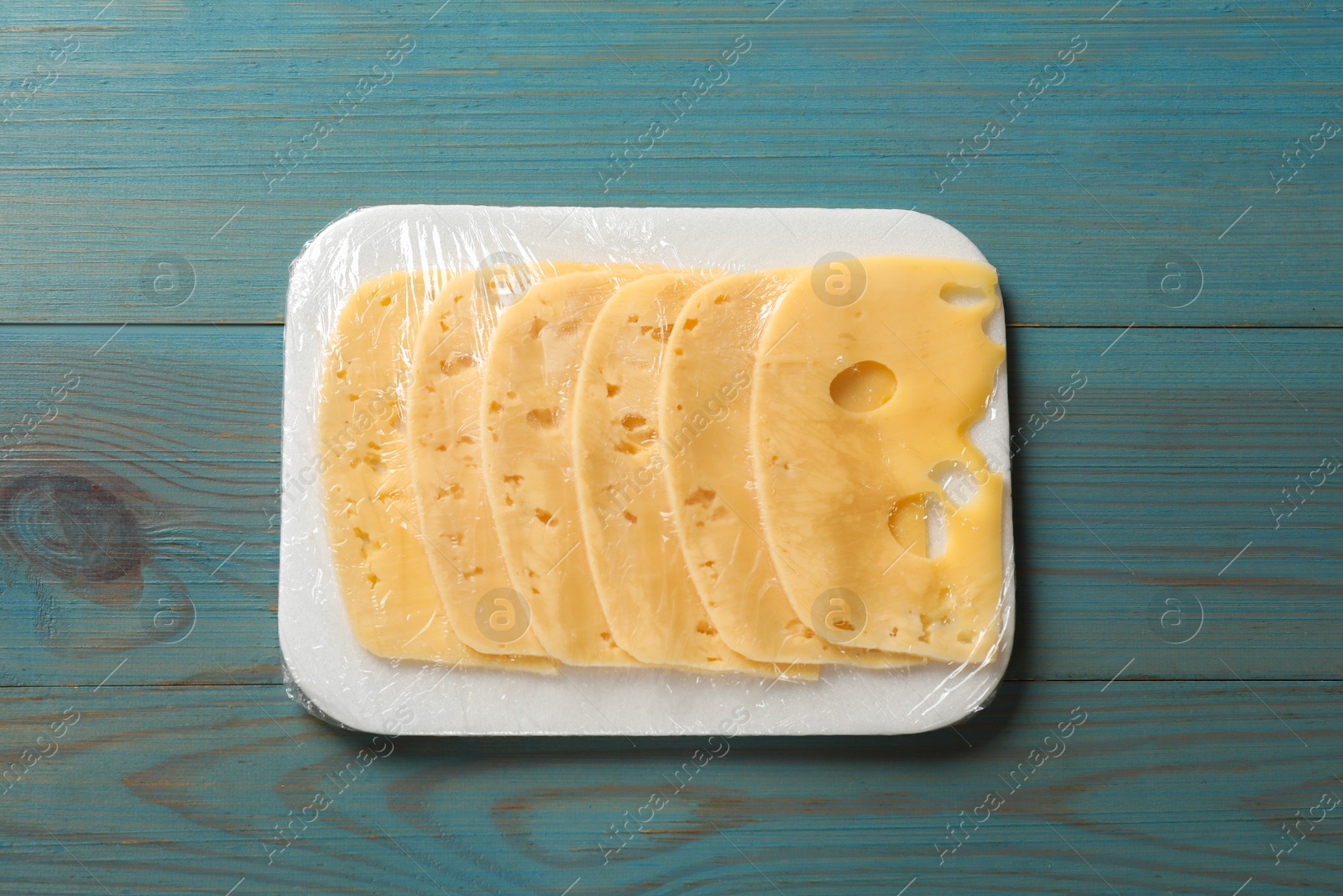 Photo of Pack of sliced cheese on light blue wooden table, top view