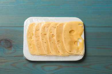 Photo of Pack of sliced cheese on light blue wooden table, top view