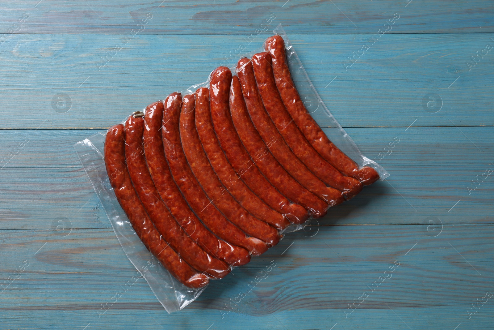 Photo of Pack of dry smoked sausages on light blue wooden table, top view