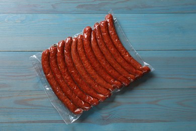 Photo of Pack of dry smoked sausages on light blue wooden table, top view