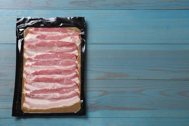 Photo of Pack of sliced bacon on light blue wooden table, top view. Space for text