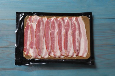 Photo of Pack of sliced bacon on light blue wooden table, top view