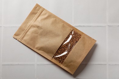 Photo of Paper pouch bag with buckwheat on white tiled table, top view