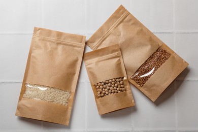 Photo of Paper pouch bags with buckwheat, chickpeas and rice on white tiled table, flat lay