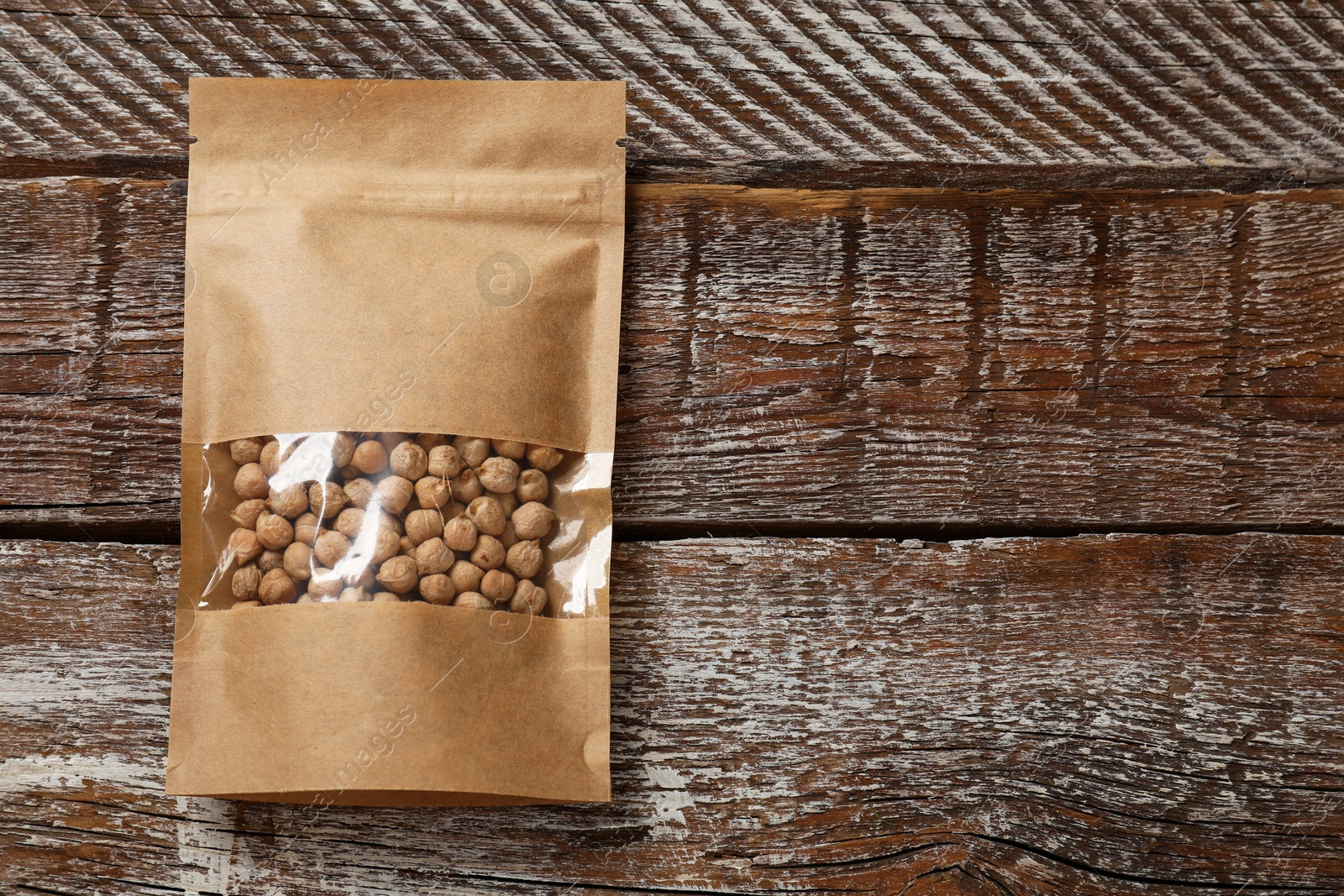 Photo of Paper pouch bag with chickpeas on wooden table, top view. Space for text