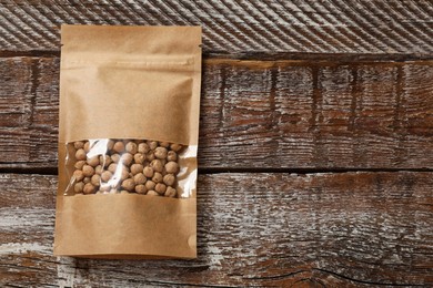 Photo of Paper pouch bag with chickpeas on wooden table, top view. Space for text