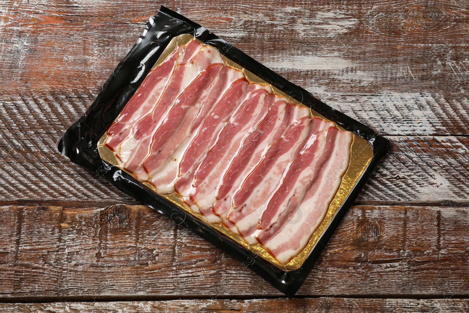 Photo of Pack of sliced bacon on wooden table, top view