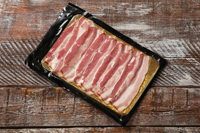 Photo of Pack of sliced bacon on wooden table, top view