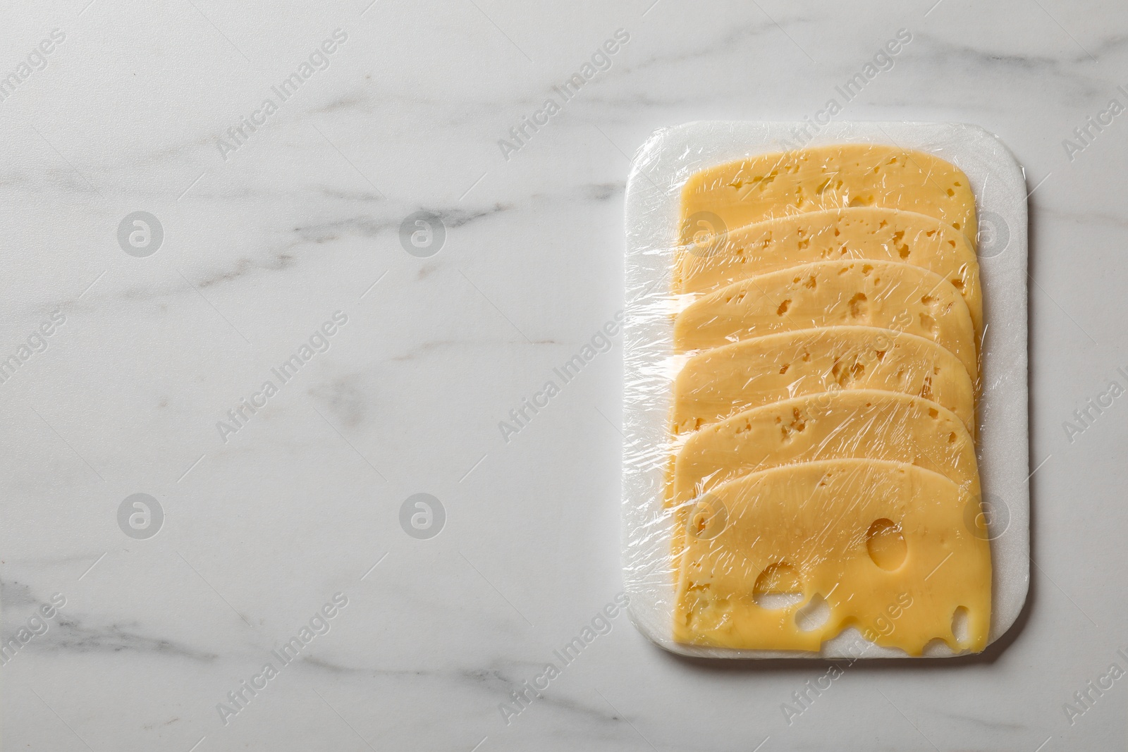 Photo of Pack of sliced cheese on white marble table, top view. Space for text