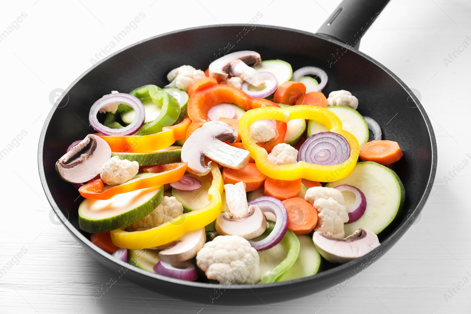 Photo of Frying pan with mix of vegetables and mushrooms on white wooden table, closeup