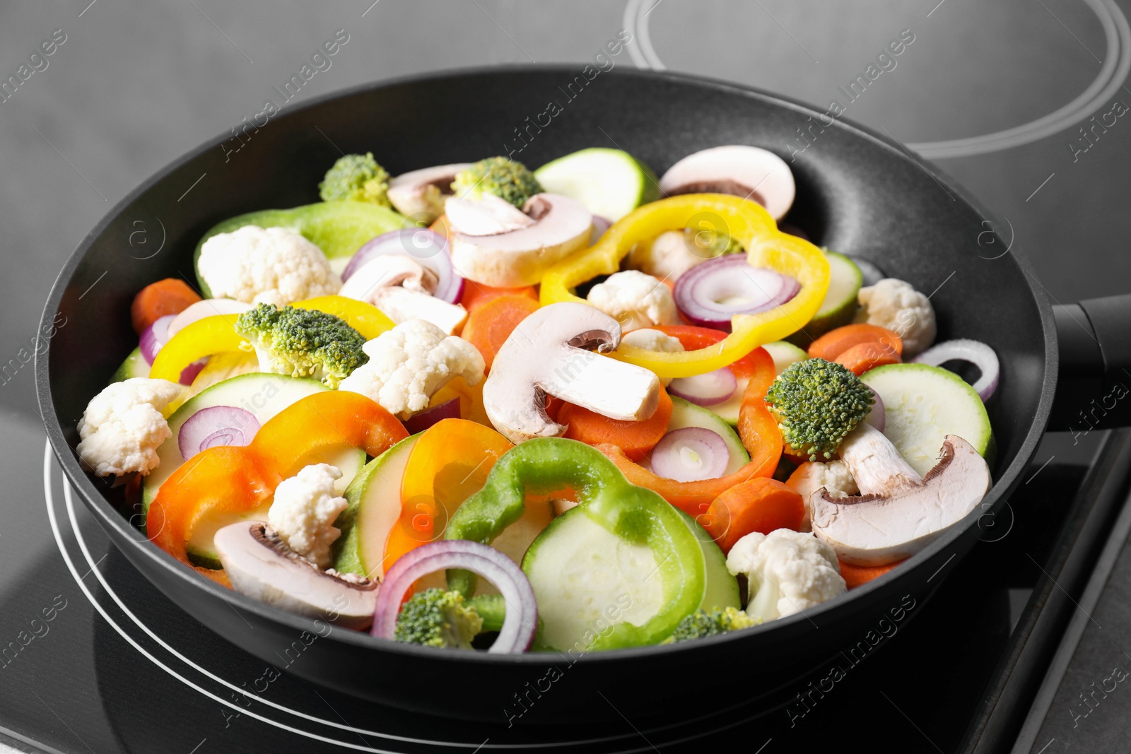 Photo of Frying pan with mix of vegetables and mushrooms on cooktop, closeup