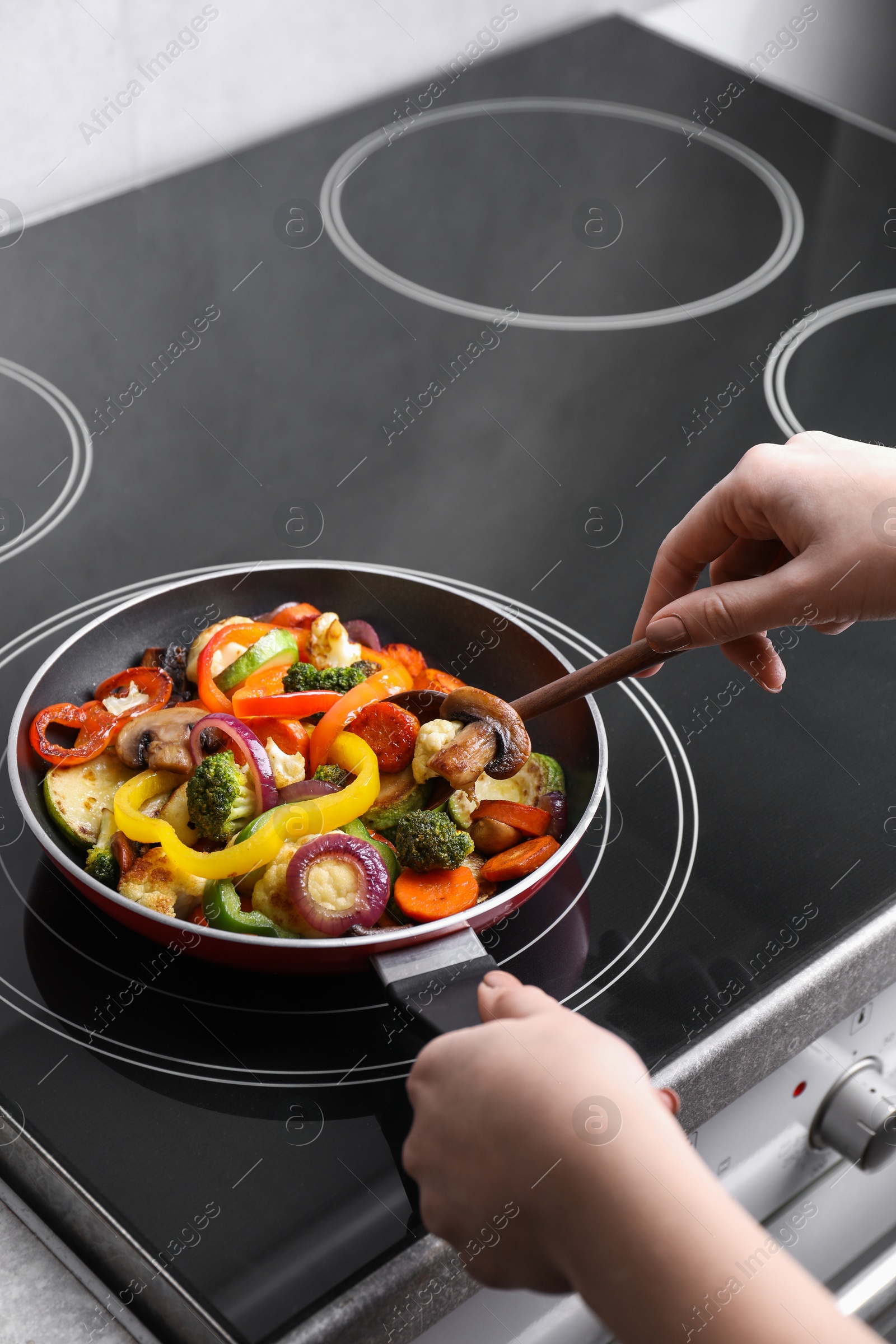 Photo of Woman cooking vegetables and mushrooms in frying pan on cooktop indoors, closeup