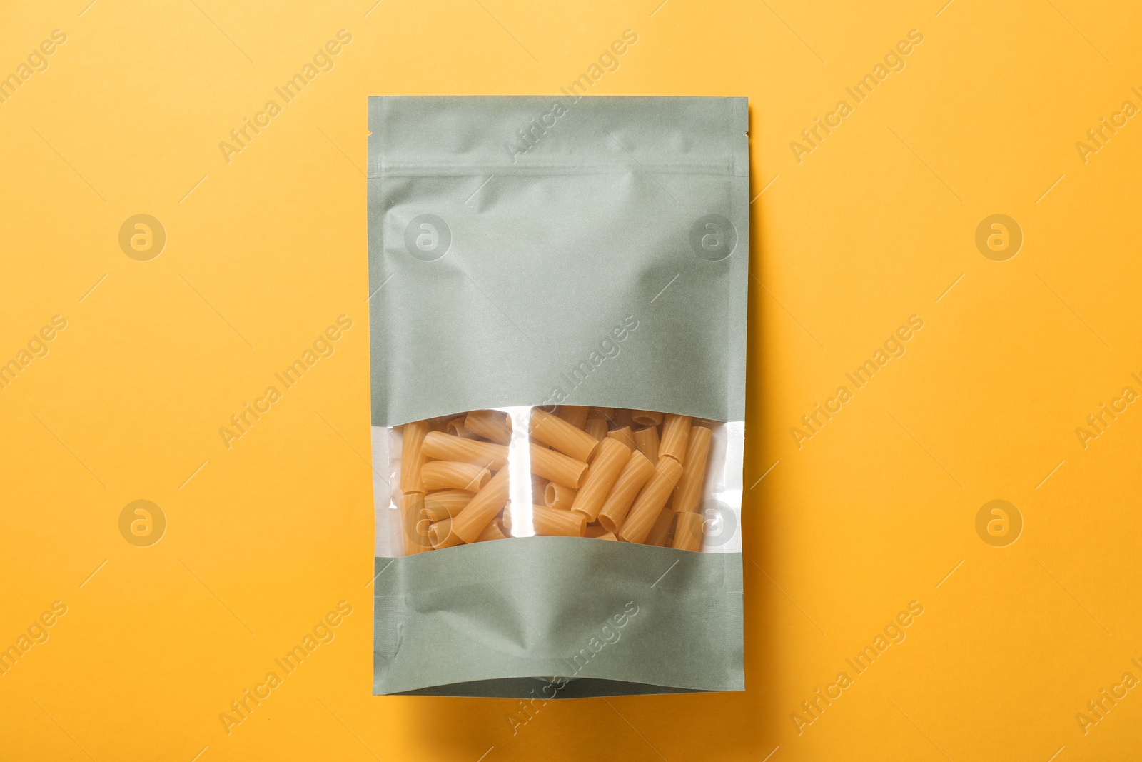 Photo of Paper pouch bag with pasta on yellow background, top view