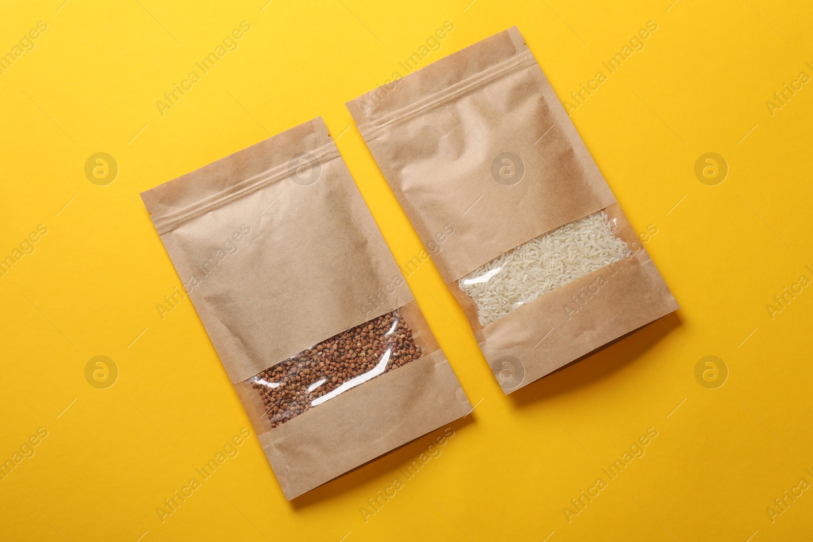 Photo of Paper pouch bags with buckwheat and rice on yellow background, top view