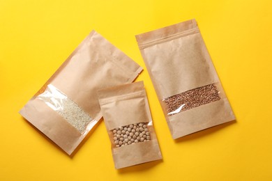 Photo of Paper pouch bags with different products on yellow background, top view