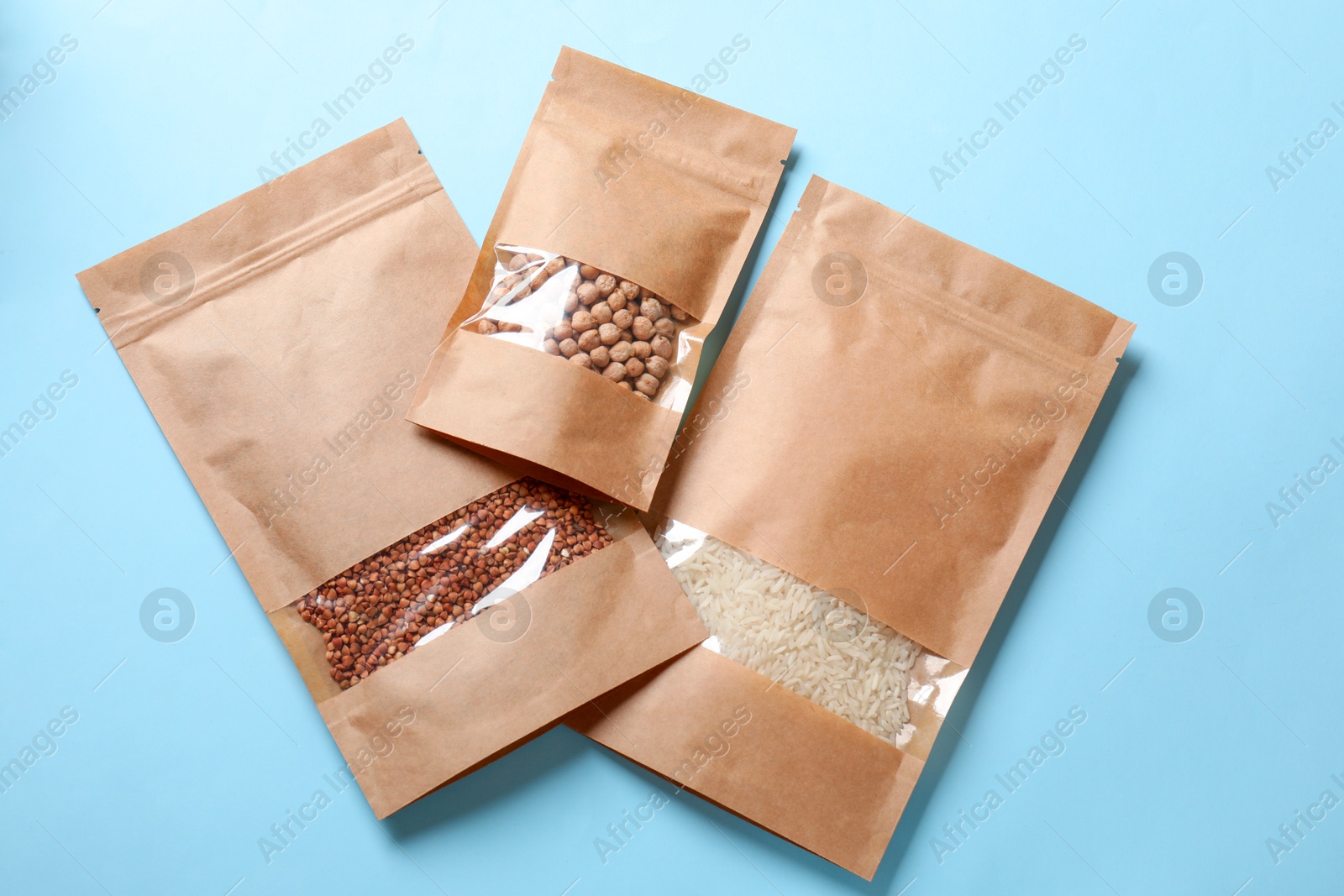 Photo of Paper pouch bags with different products on light blue background, top view