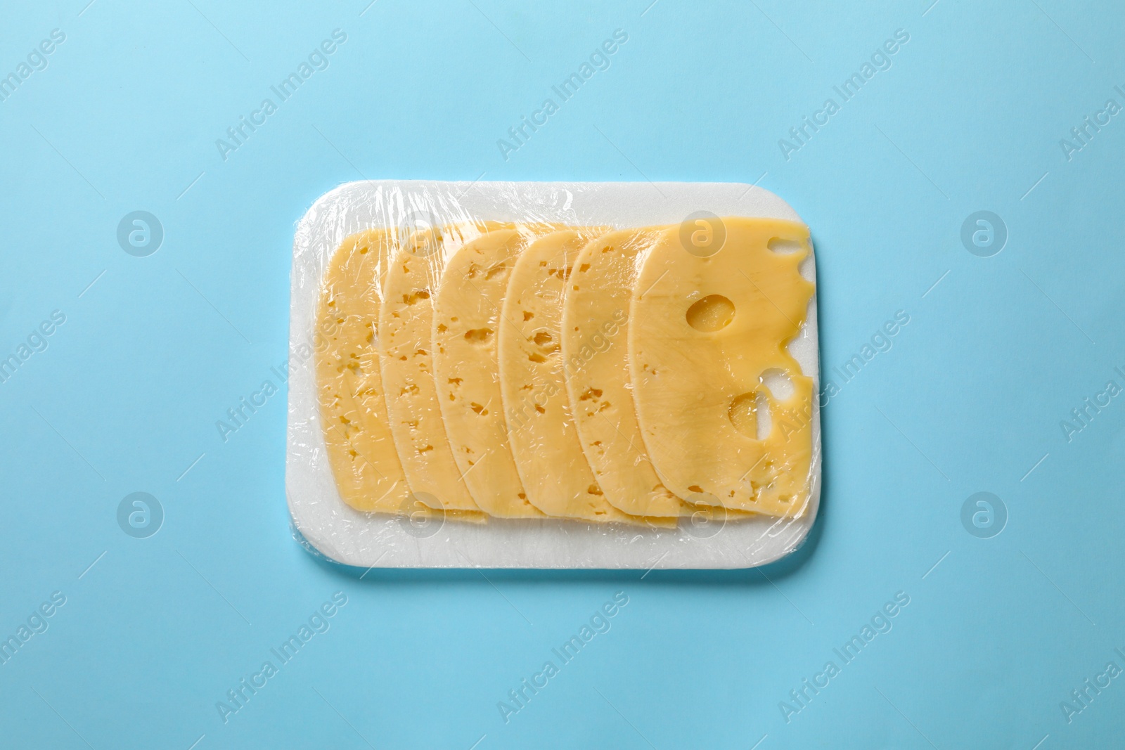 Photo of Pack of sliced cheese on light blue background, top view