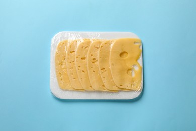 Pack of sliced cheese on light blue background, top view