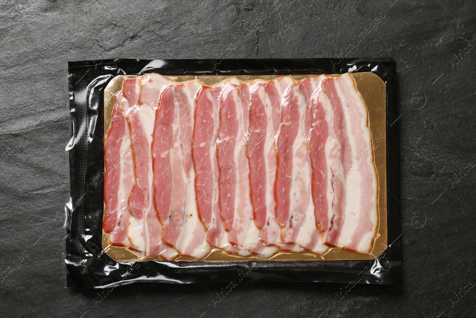 Photo of Pack of sliced bacon on black table, top view