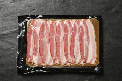 Photo of Pack of sliced bacon on black table, top view