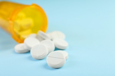 Photo of Bottle of antibiotic pills on light blue background, closeup. Space for text