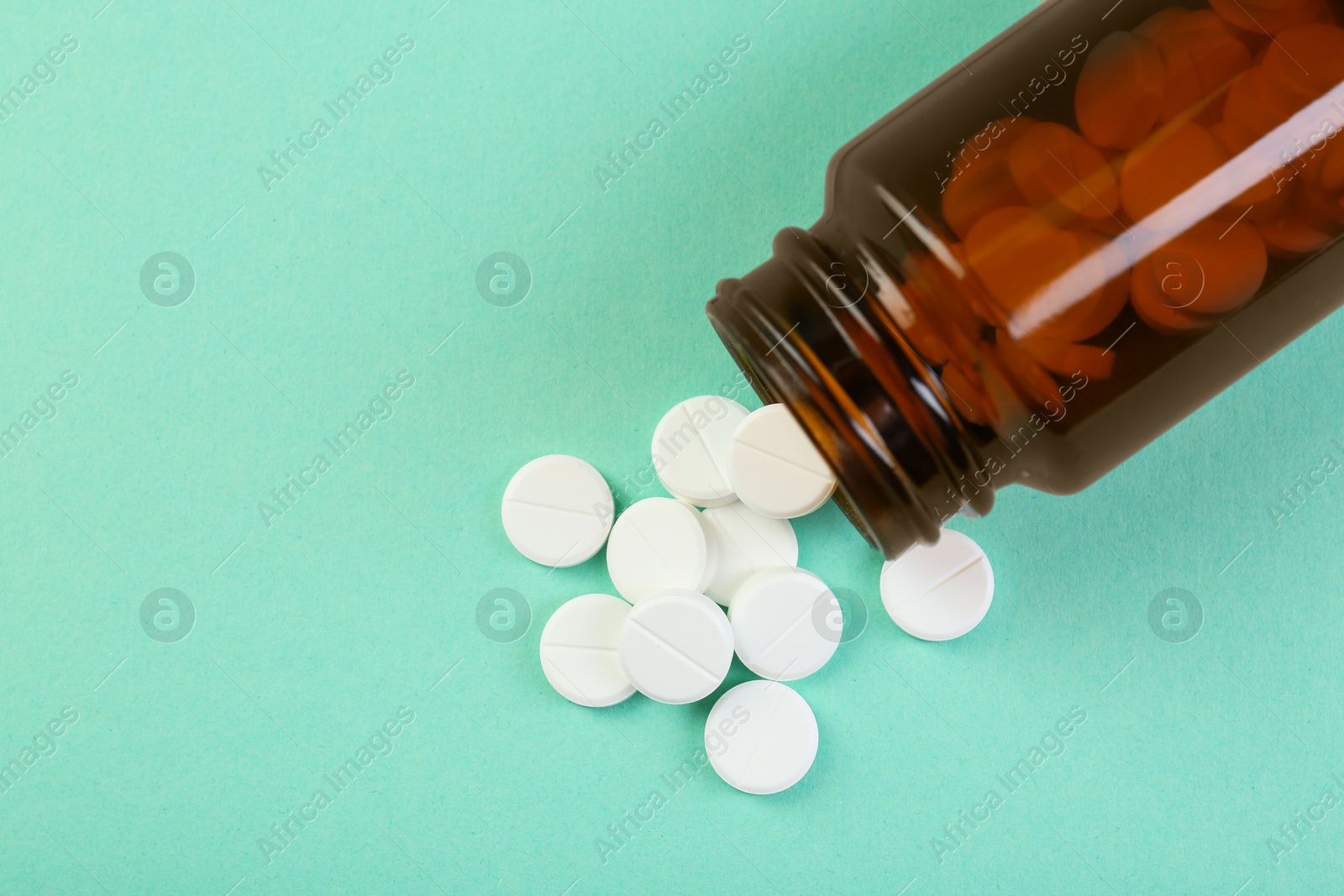 Photo of Bottle of antibiotic pills on turquoise background, top view. Space for text