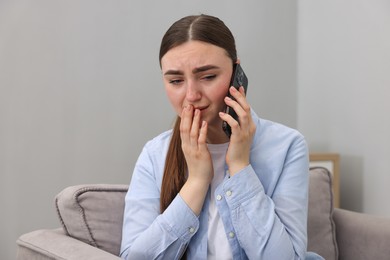 Photo of Stressed woman calling hotline for mental health help in armchair at home