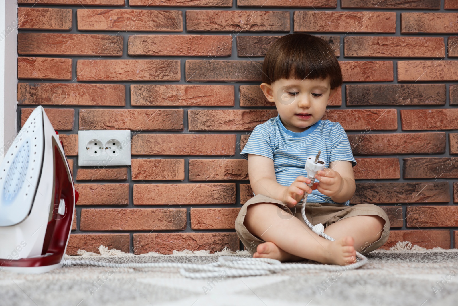 Photo of Little boy playing with iron plug near electrical socket at home. Child in danger