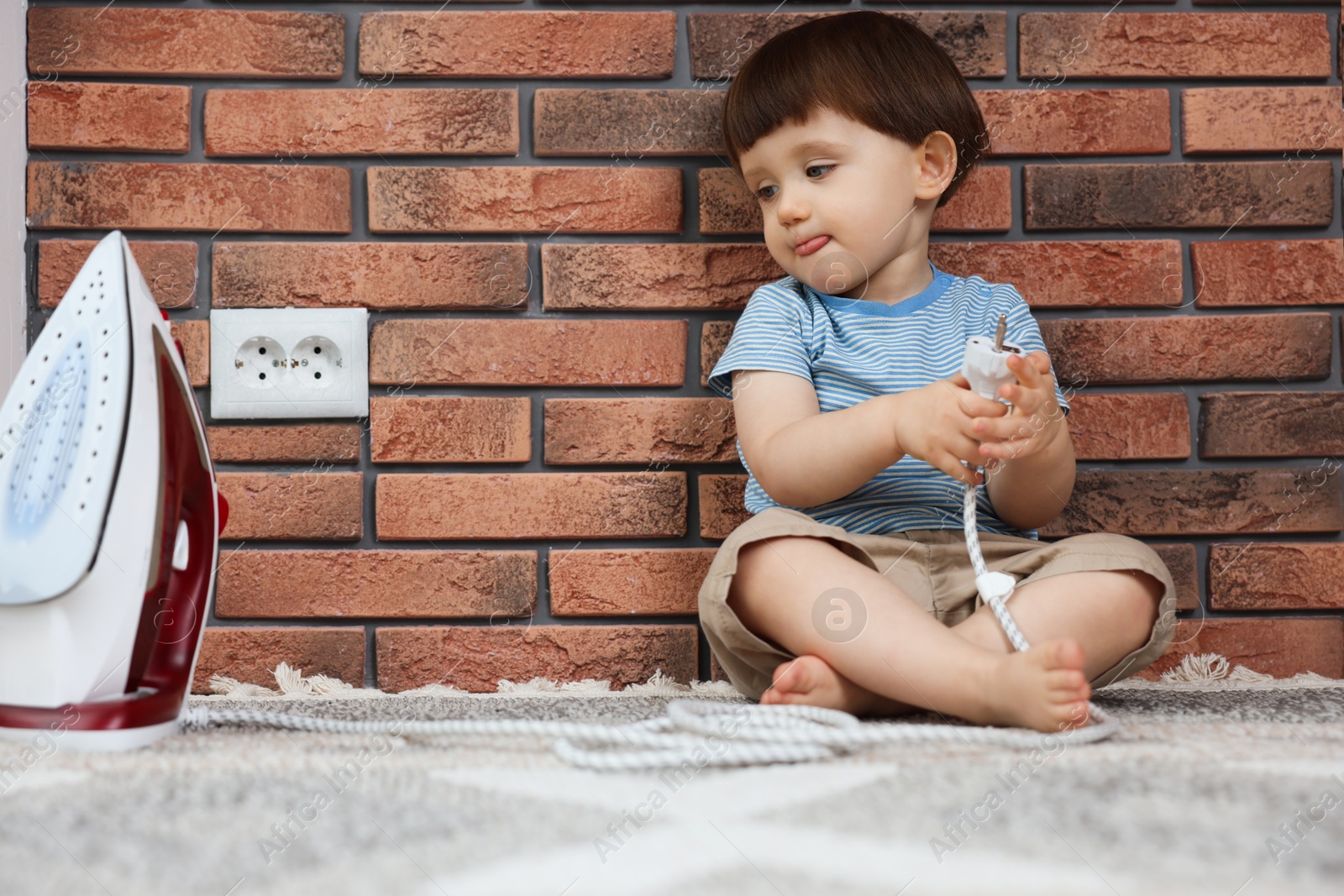 Photo of Little boy playing with iron plug near electrical socket at home. Child in danger