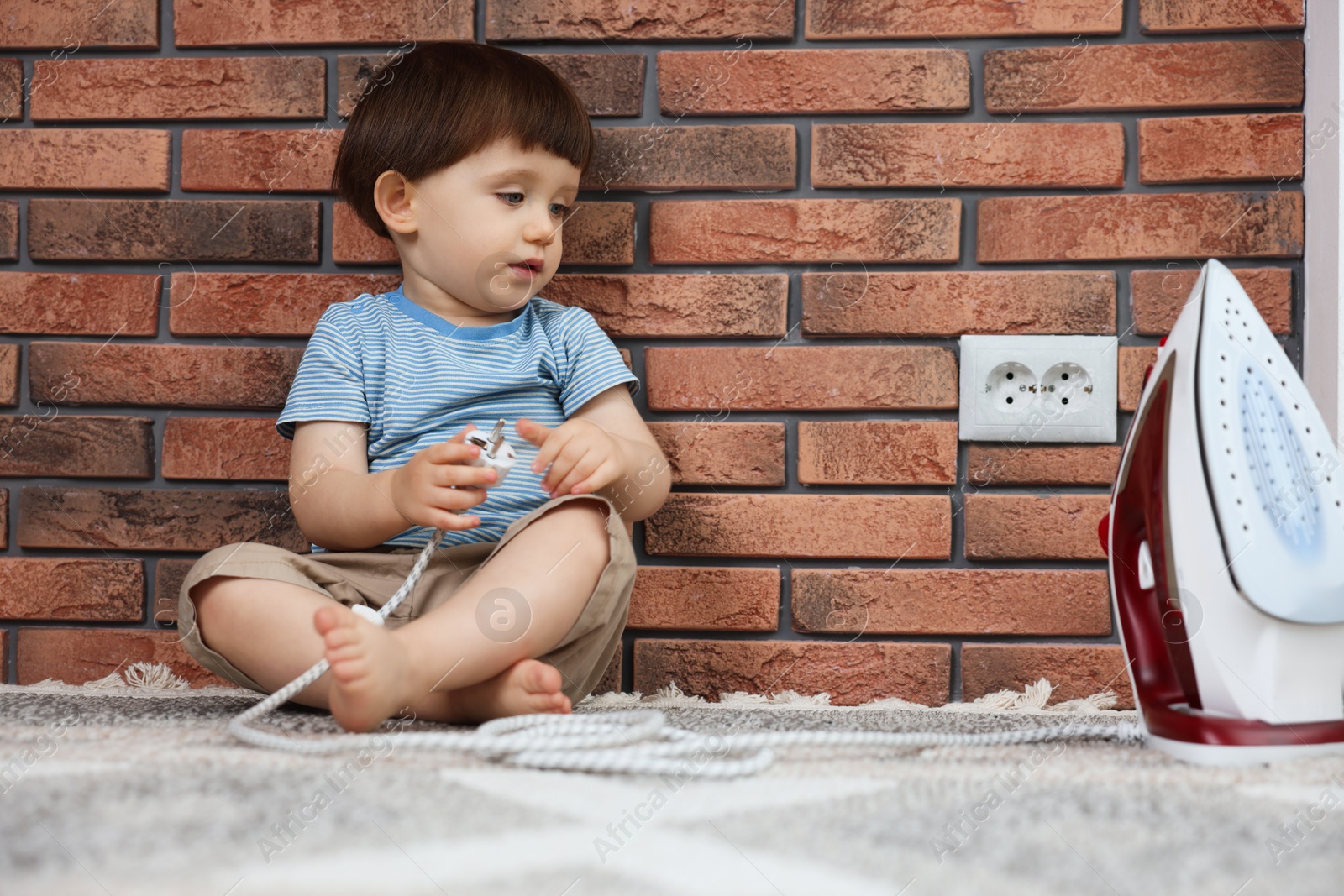 Photo of Little boy playing with iron plug near electrical socket at home. Child in danger