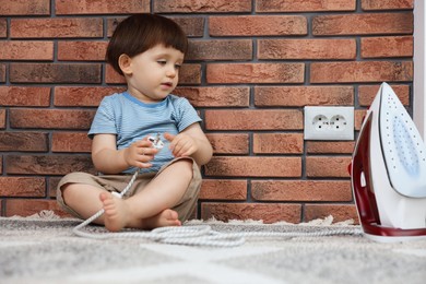 Photo of Little boy playing with iron plug near electrical socket at home. Child in danger