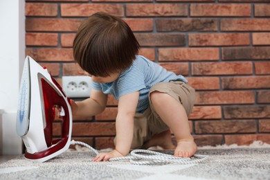 Photo of Little boy playing with iron at home. Child in danger