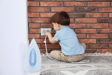 Little boy playing with iron plug and electrical socket at home, back view. Child in danger