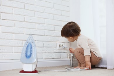 Photo of Little boy playing with iron plug and electrical socket at home. Child in danger