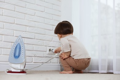 Photo of Little boy playing with iron plug and electrical socket at home. Child in danger