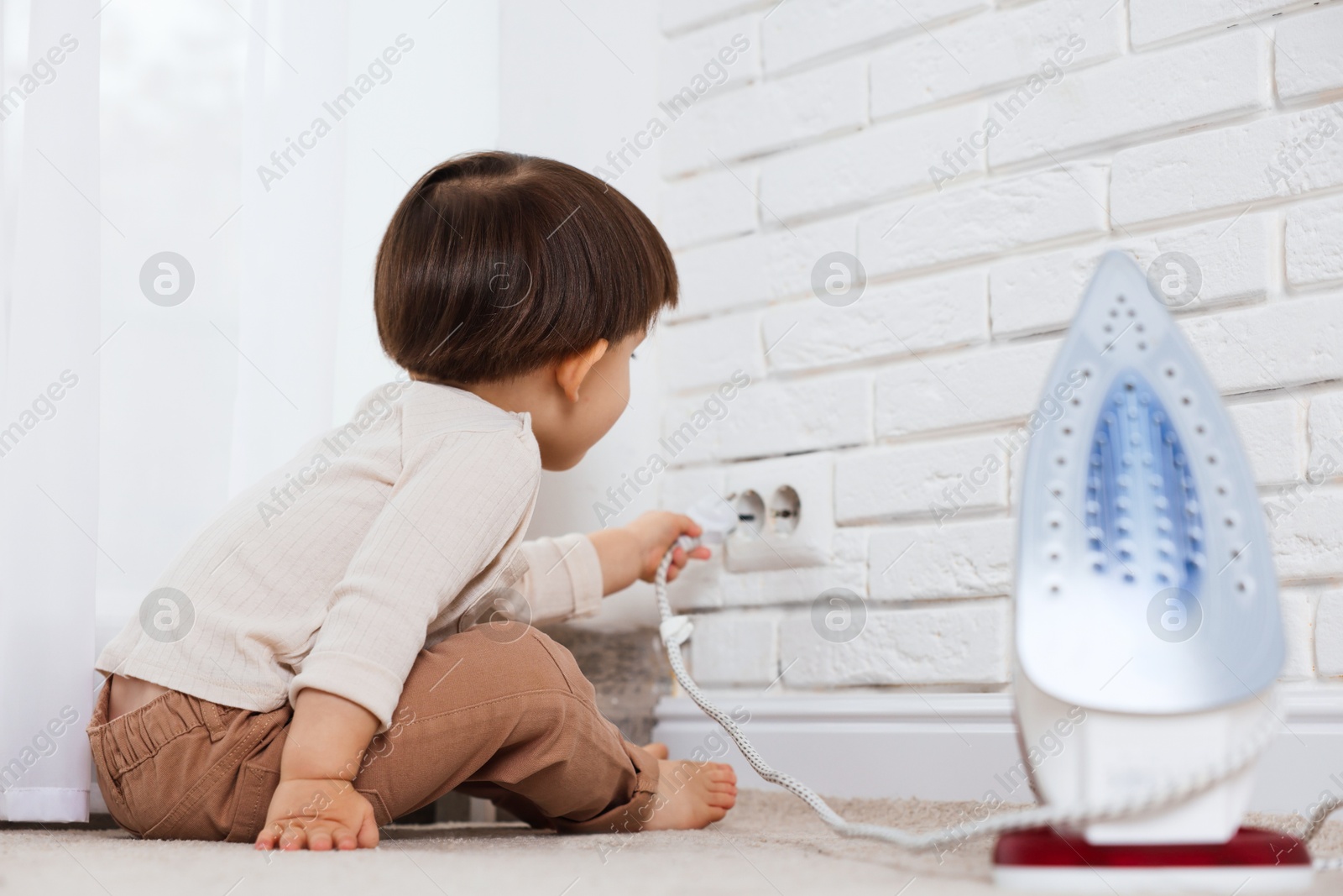 Photo of Little boy playing with iron plug and electrical socket at home. Child in danger