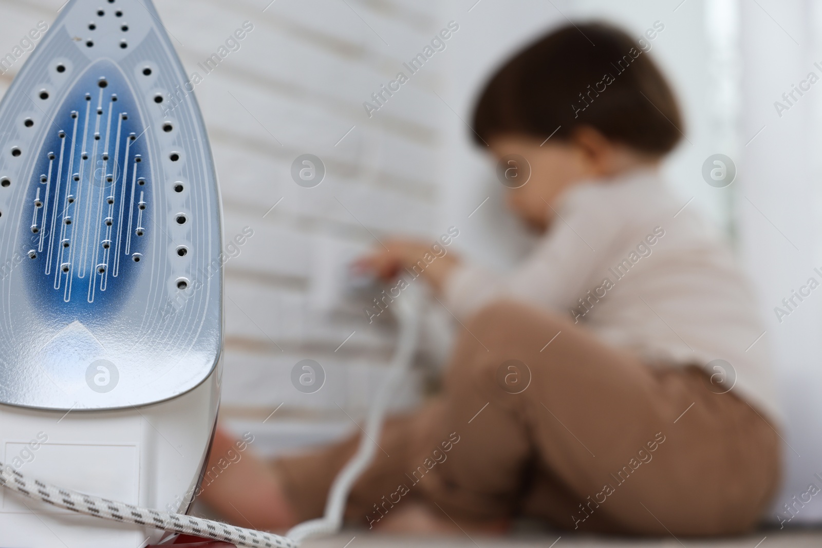 Photo of Little boy playing with iron plug and electrical socket at home, selective focus. Child in danger